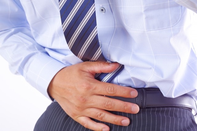 下腹部をおさえるスーツ男性